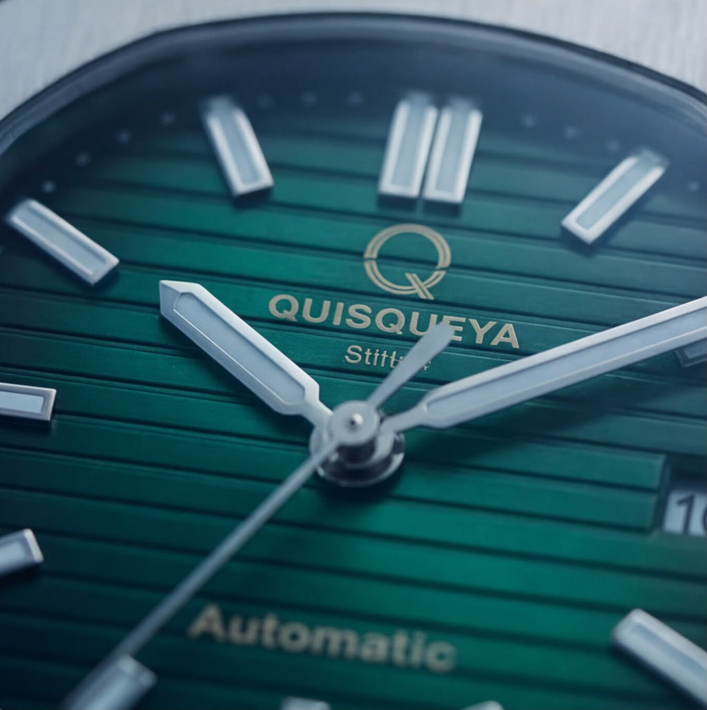 Close-up of a Quisqueya automatic watch dial with a green textured background, silver baton hour markers, and gold-toned brand lettering.