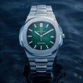 A Quisqueya Stellar automatic wristwatch with a brushed silver-tone stainless steel case and integrated bracelet, featuring a vibrant green dial and silver-tone hour markers, shown against a dark, water-textured background.